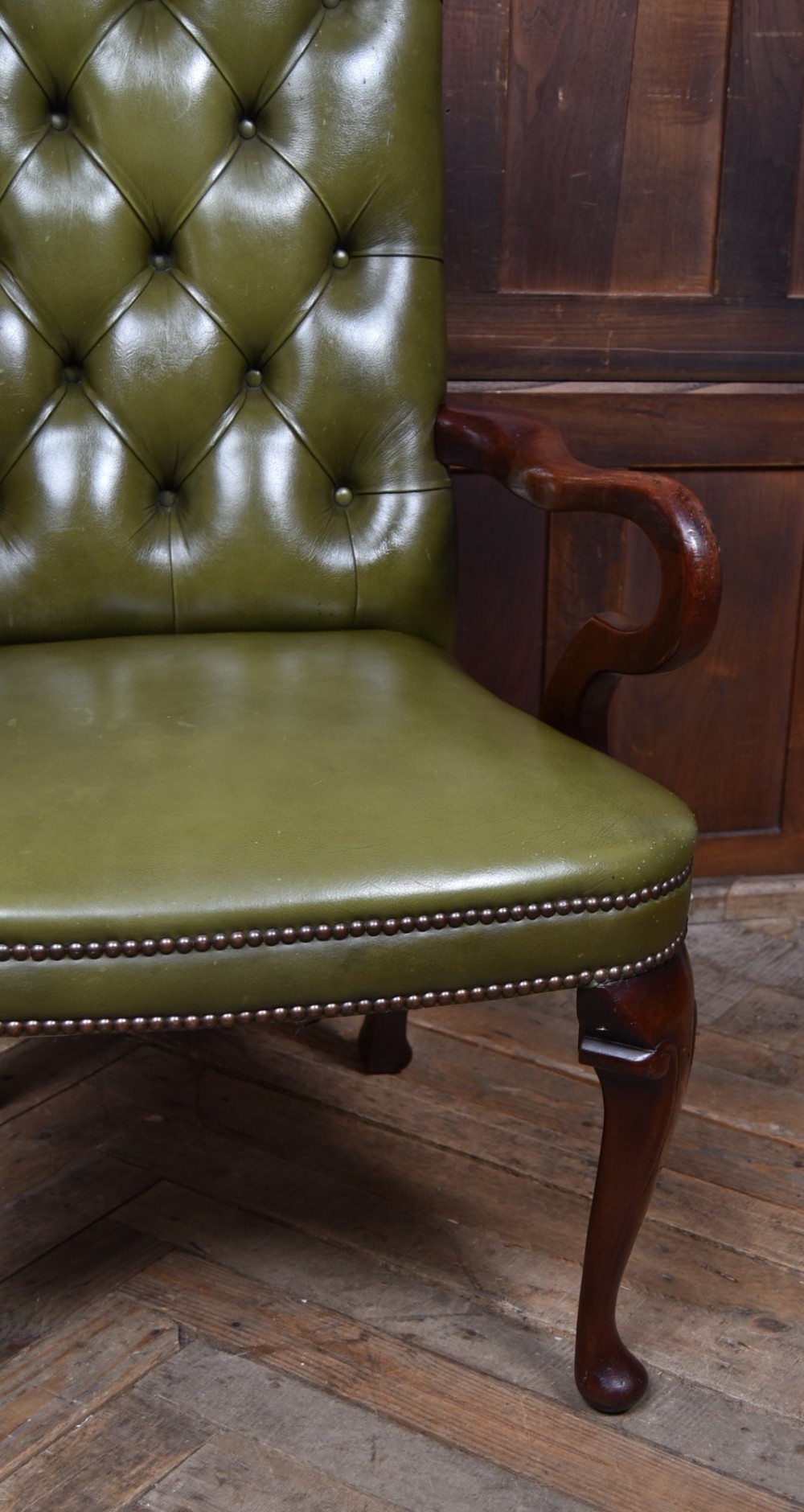 A high-backed desk chair featuring olive green button-tufted leather upholstery, carved dark wood armrests, brass stud trimming, and front cabriole legs. View IV