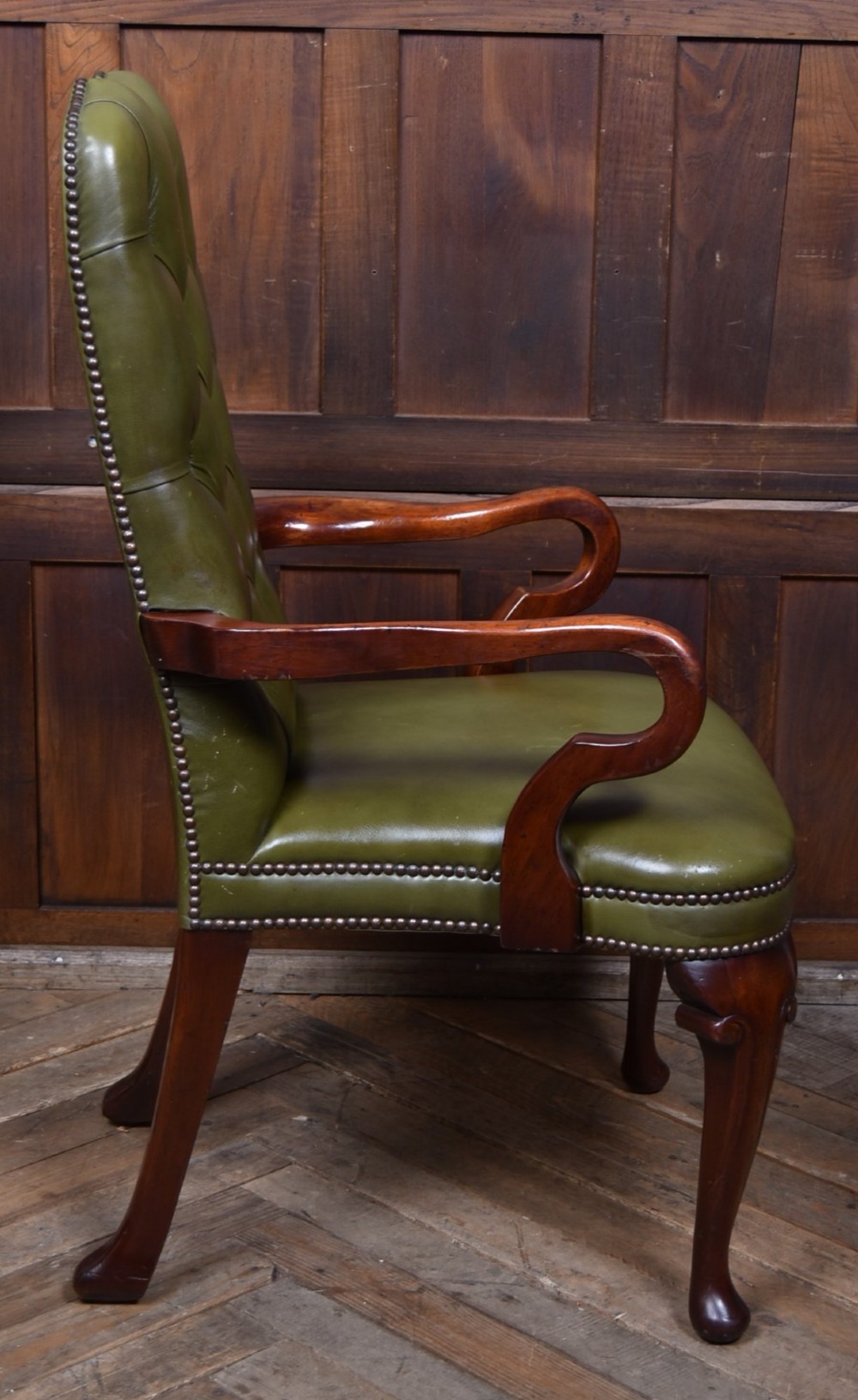 A high-backed desk chair featuring olive green button-tufted leather upholstery, carved dark wood armrests, brass stud trimming, and front cabriole legs. View VIII
