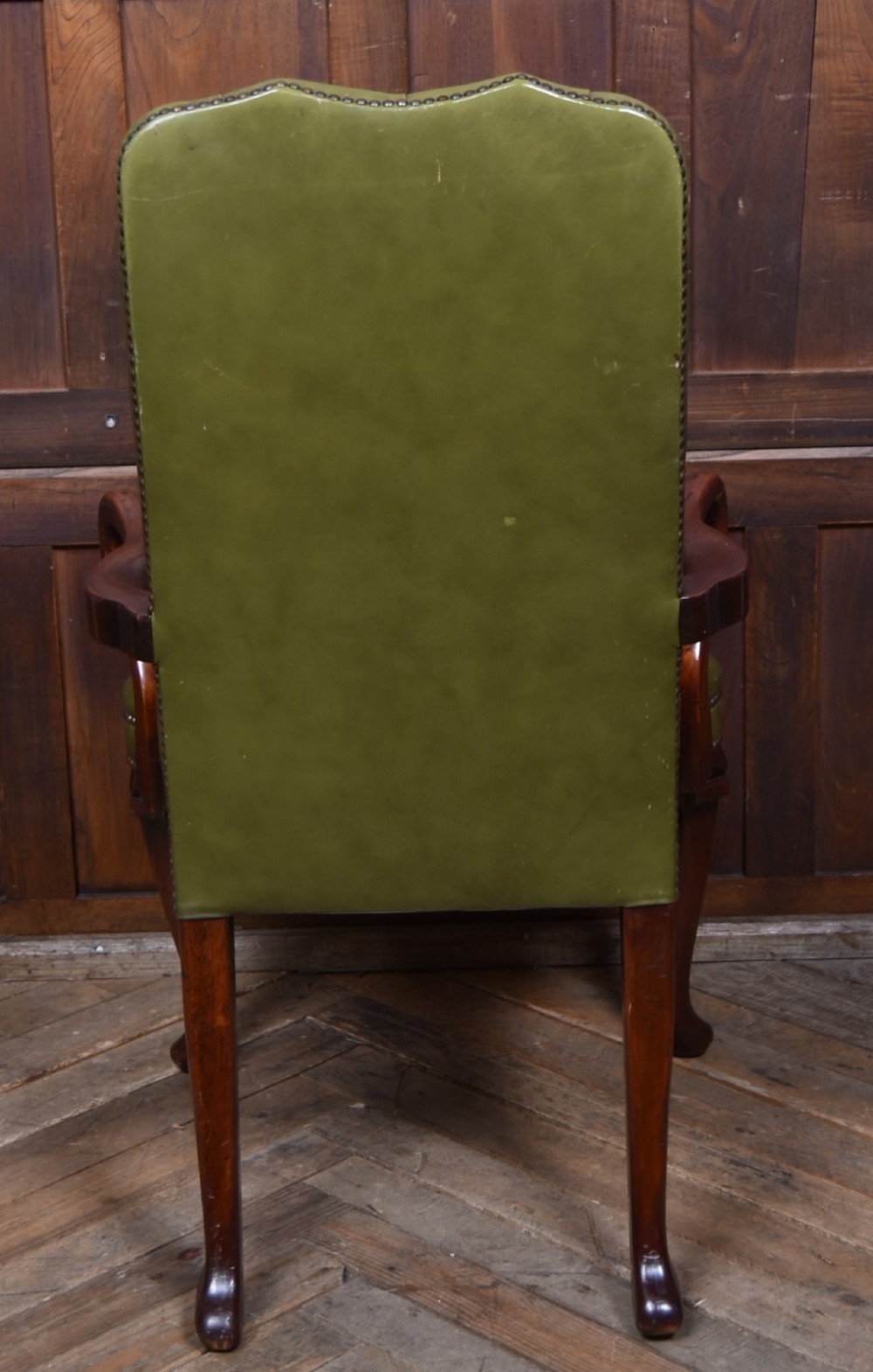 A high-backed desk chair featuring olive green button-tufted leather upholstery, carved dark wood armrests, brass stud trimming, and front cabriole legs. View IX