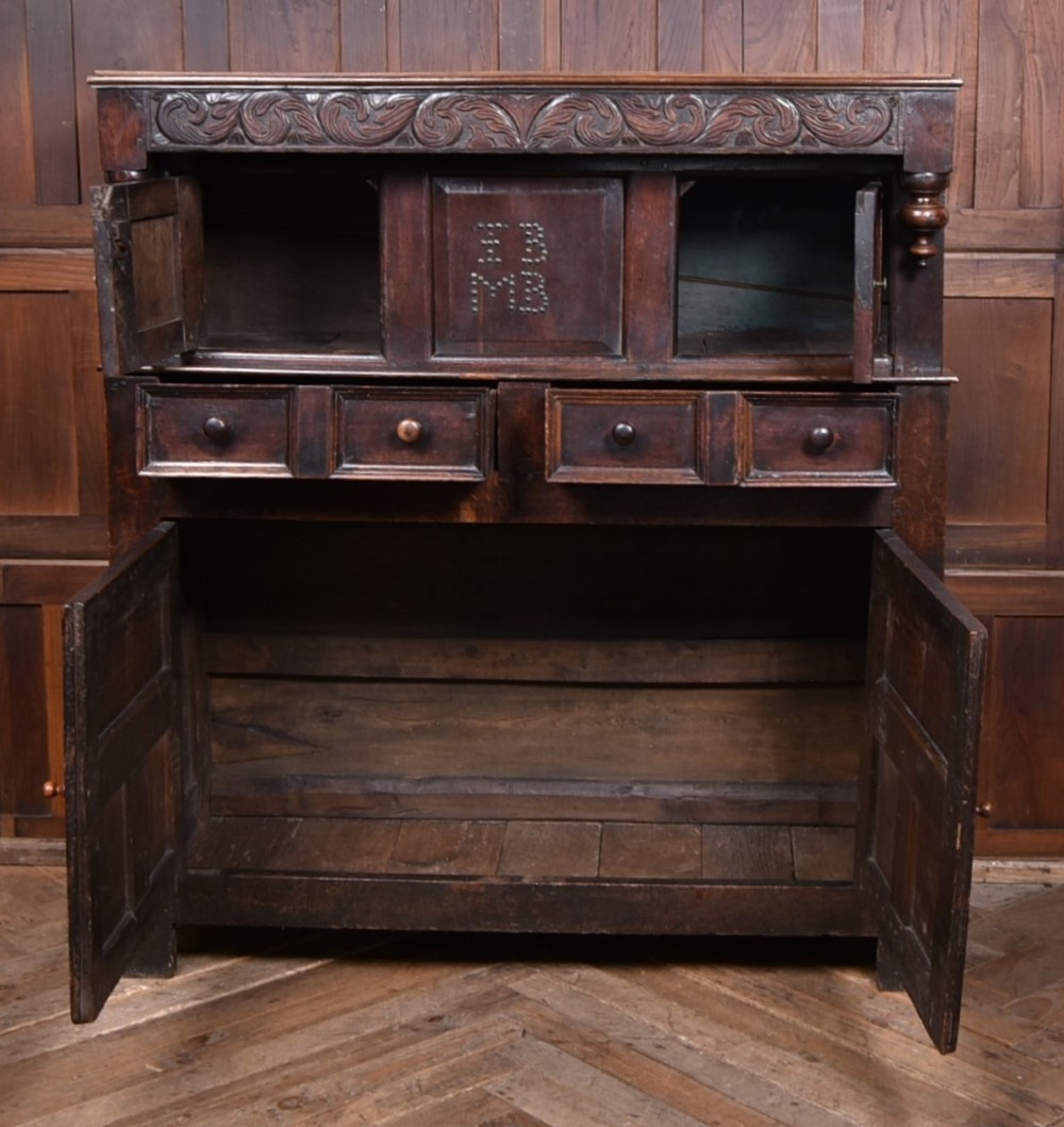 A 17th-century dark oak court cupboard featuring a carved lunette frieze, turned drop pendants, studded panel initials, and geometric lower doors. View III