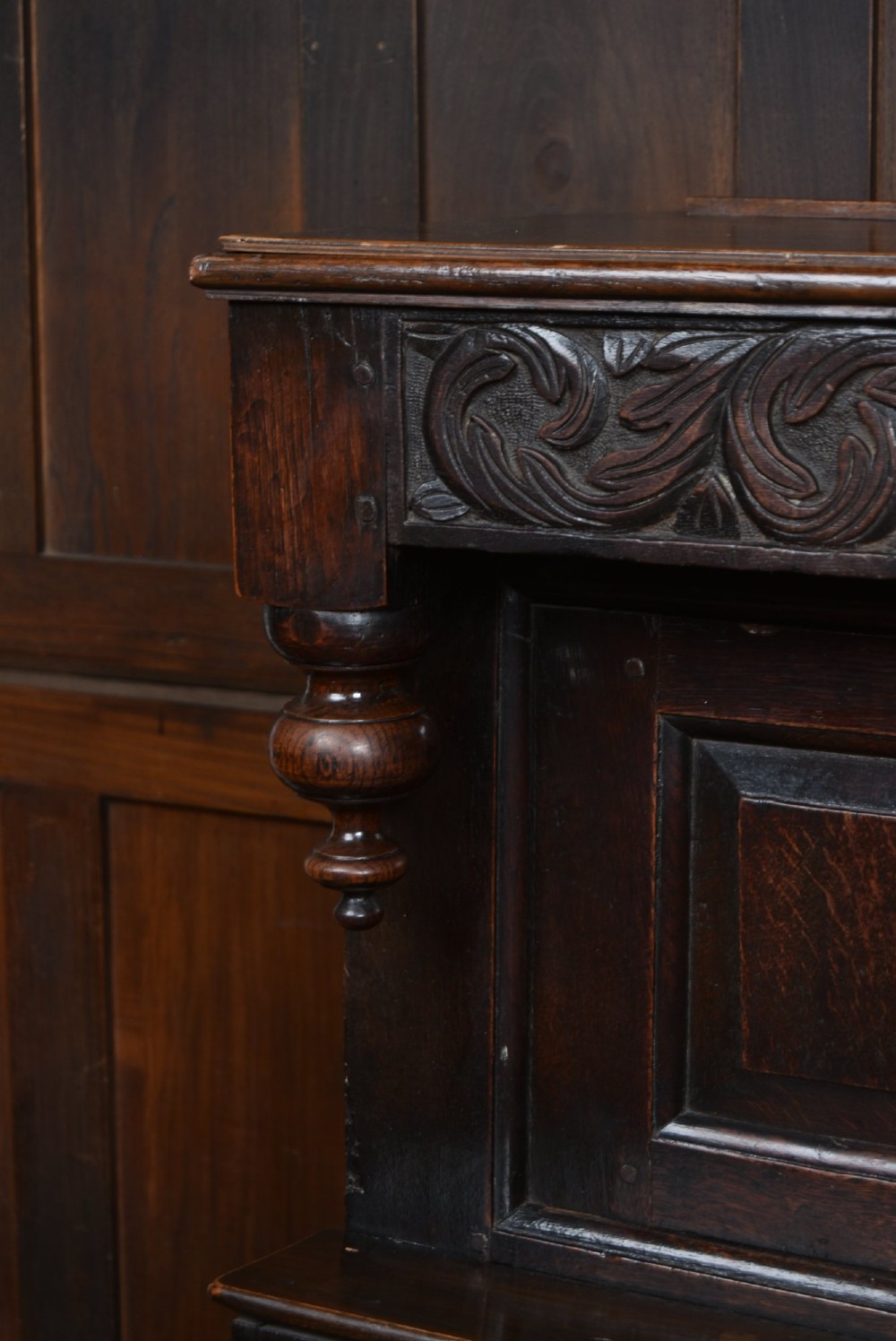 A 17th-century dark oak court cupboard featuring a carved lunette frieze, turned drop pendants, studded panel initials, and geometric lower doors. View VI
