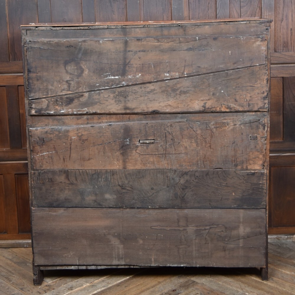 A 17th-century dark oak court cupboard featuring a carved lunette frieze, turned drop pendants, studded panel initials, and geometric lower doors. View IX