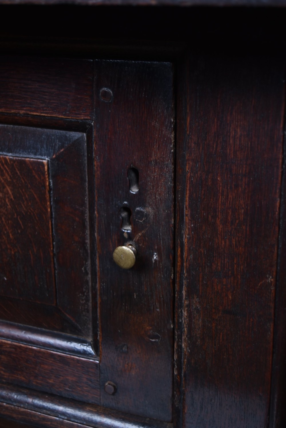 A 17th-century dark oak court cupboard featuring a carved lunette frieze, turned drop pendants, studded panel initials, and geometric lower doors. View XI
