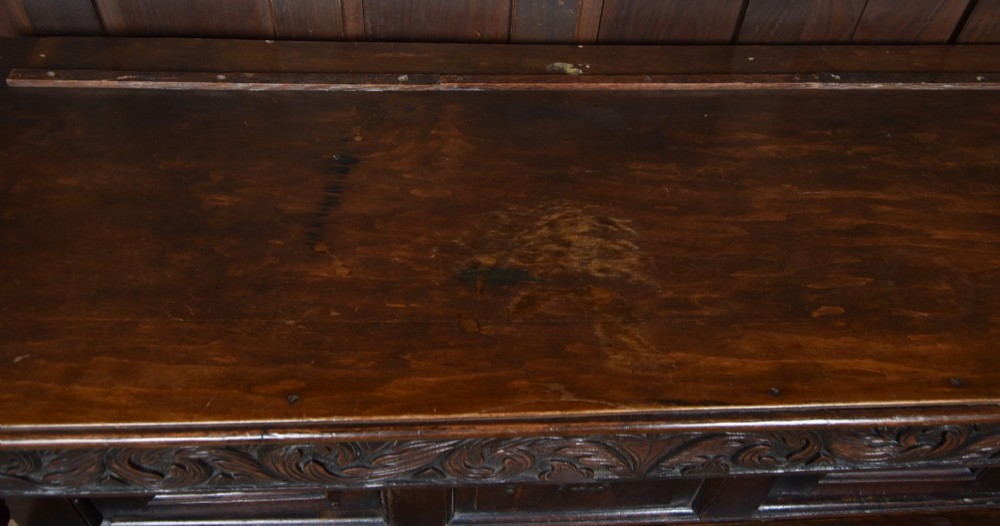 A 17th-century dark oak court cupboard featuring a carved lunette frieze, turned drop pendants, studded panel initials, and geometric lower doors. View XII
