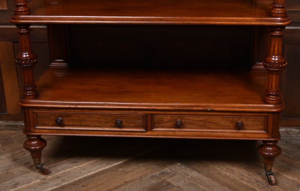 A Victorian mahogany three-tiered whatnot featuring turned column supports, two lower drawers with knob handles, an arched gallery top, and brass castors. View V