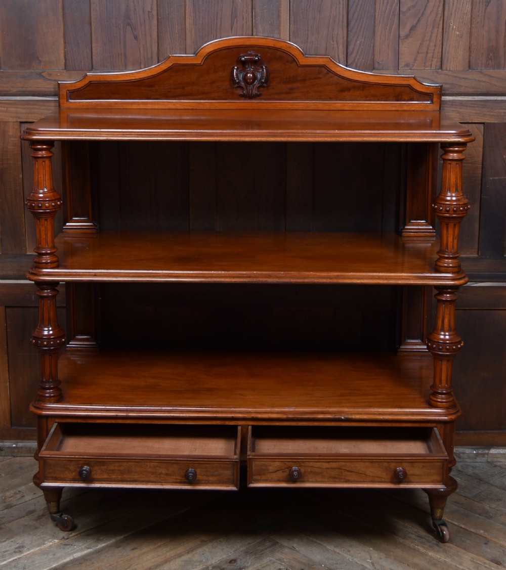 A Victorian mahogany three-tiered whatnot featuring turned column supports, two lower drawers with knob handles, an arched gallery top, and brass castors. View VI