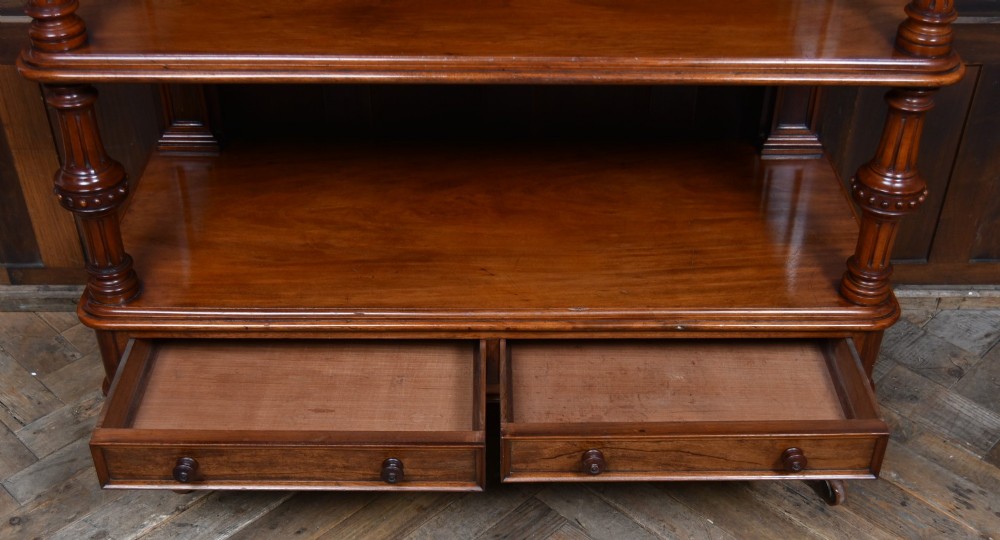 A Victorian mahogany three-tiered whatnot featuring turned column supports, two lower drawers with knob handles, an arched gallery top, and brass castors. View VII
