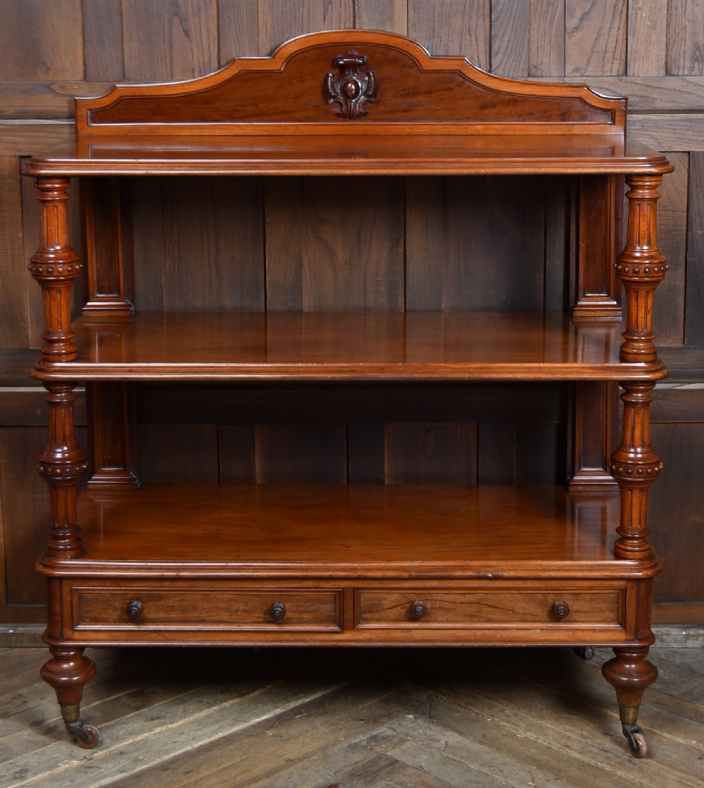 A Victorian mahogany three-tiered whatnot featuring turned column supports, two lower drawers with knob handles, an arched gallery top, and brass castors. View VIII