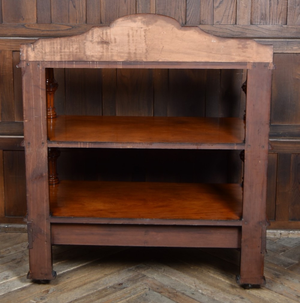 A Victorian mahogany three-tiered whatnot featuring turned column supports, two lower drawers with knob handles, an arched gallery top, and brass castors. View X