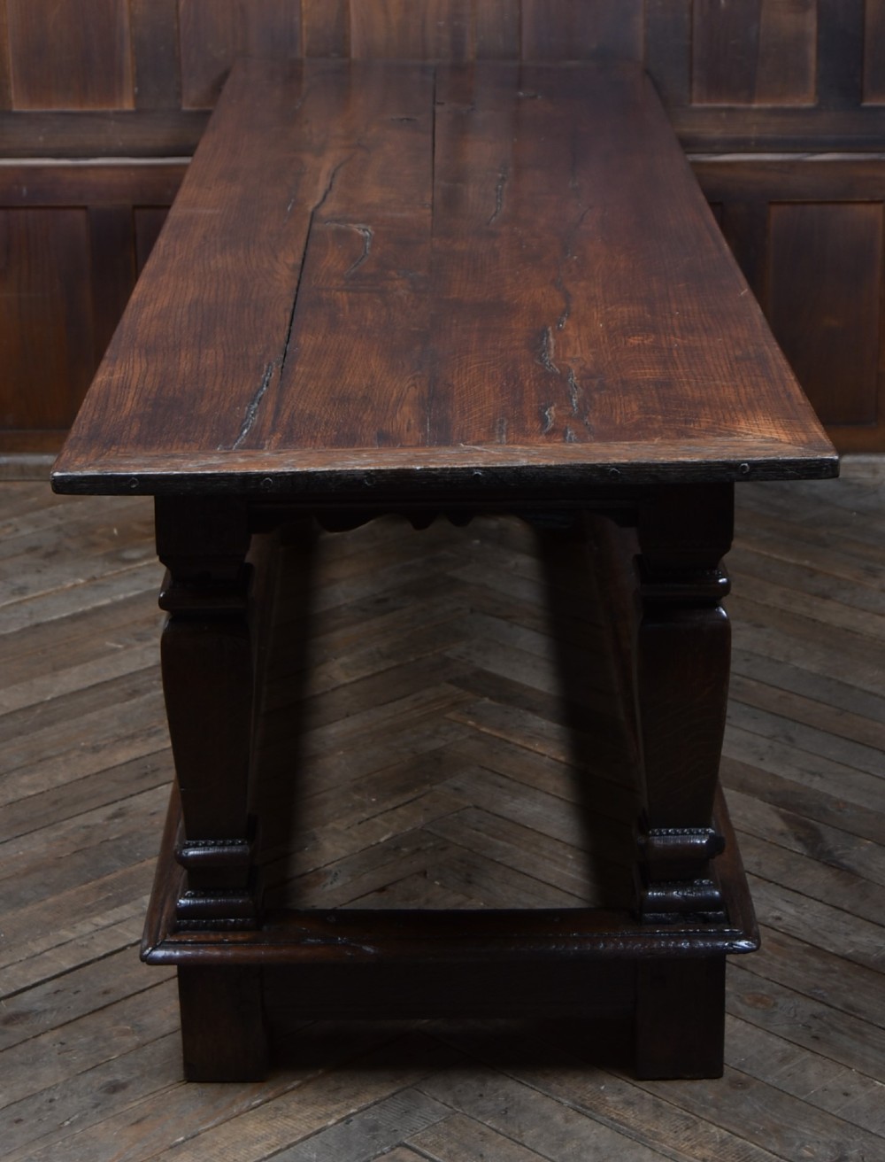 An 18th-century dark oak refectory dining table featuring a long plank top, scalloped apron carving, turned legs, and low foot stretchers. View II