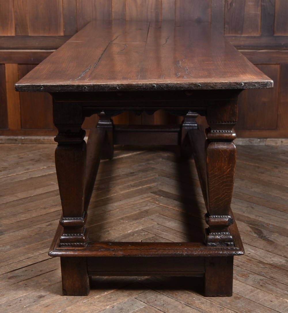 An 18th-century dark oak refectory dining table featuring a long plank top, scalloped apron carving, turned legs, and low foot stretchers. View IV