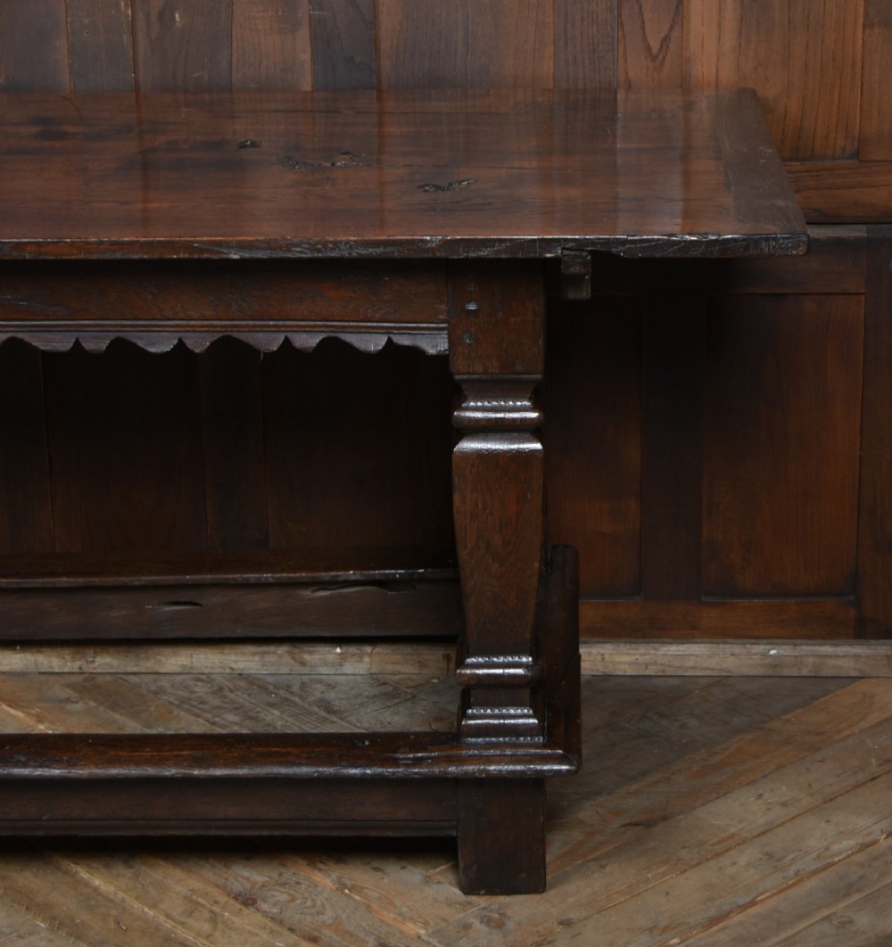An 18th-century dark oak refectory dining table featuring a long plank top, scalloped apron carving, turned legs, and low foot stretchers. View VIII