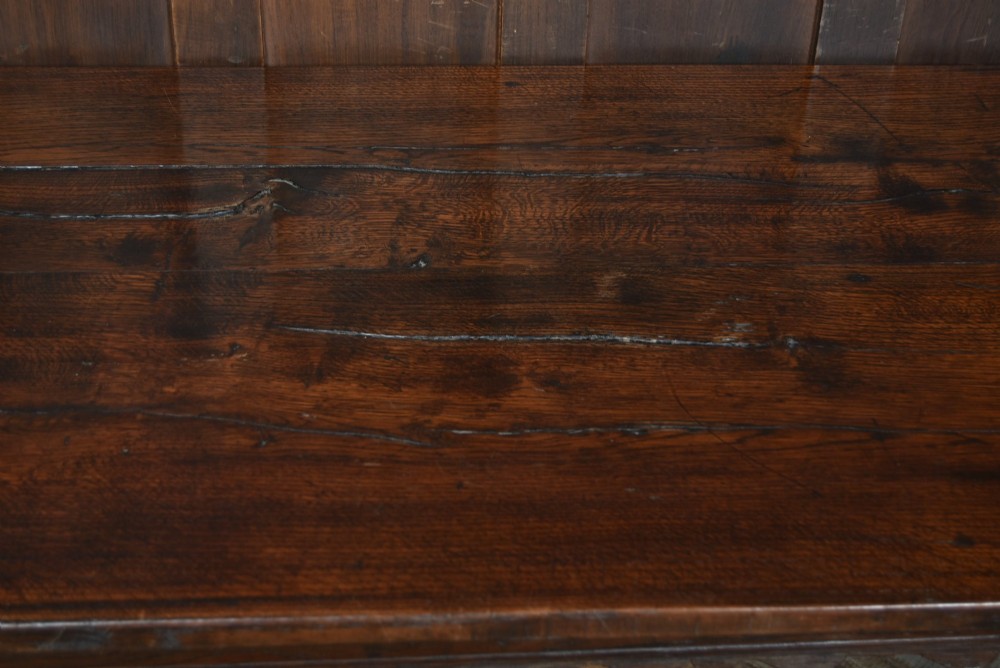 An 18th-century dark oak refectory dining table featuring a long plank top, scalloped apron carving, turned legs, and low foot stretchers. View IX