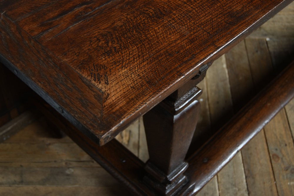 An 18th-century dark oak refectory dining table featuring a long plank top, scalloped apron carving, turned legs, and low foot stretchers. View XI