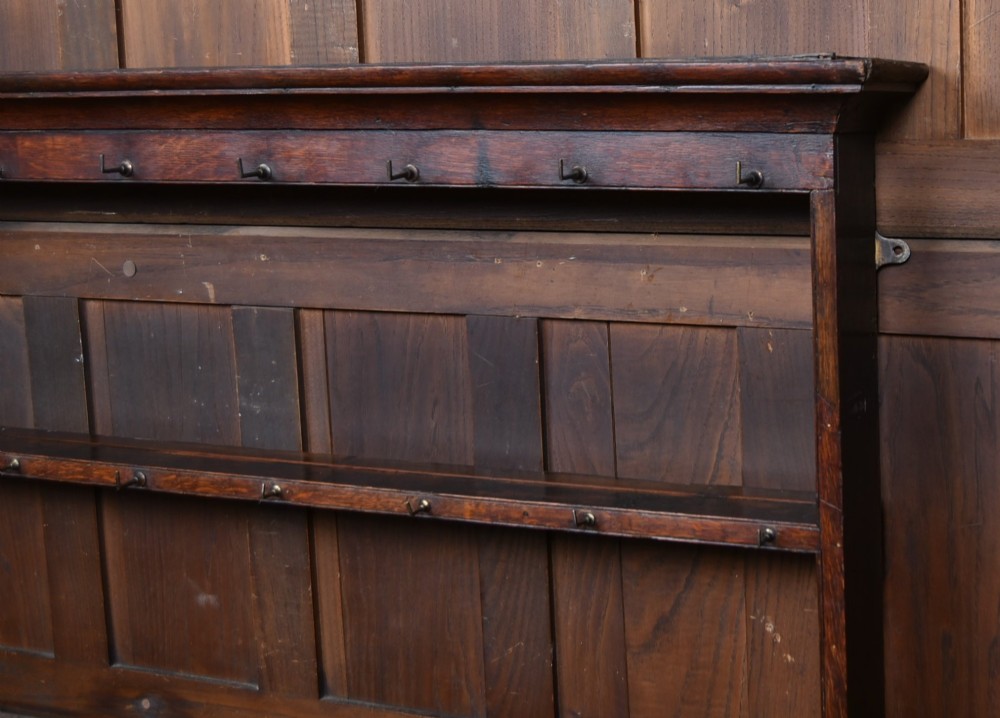 A dark patinated oak country dresser featuring a three-tiered open plate rack stacked with ceramic tableware, set above a base with five drawers, turned front legs, and a low pot board shelf. View III