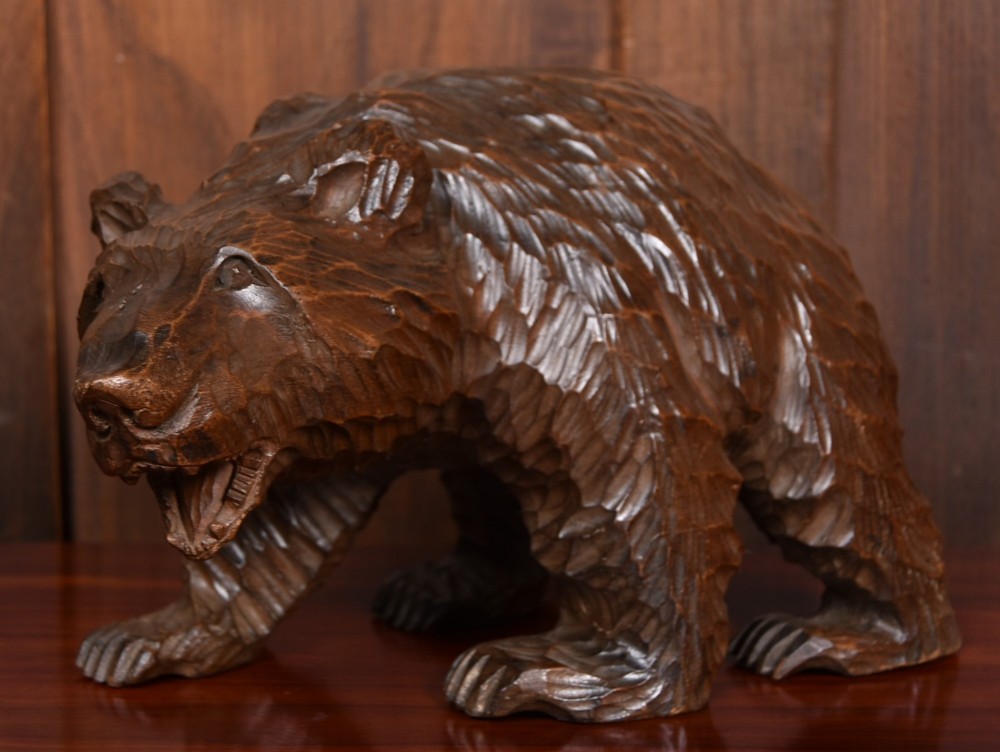 A hand-carved dark wood bear sculpture featuring detailed gouged fur texture and an open mouth.