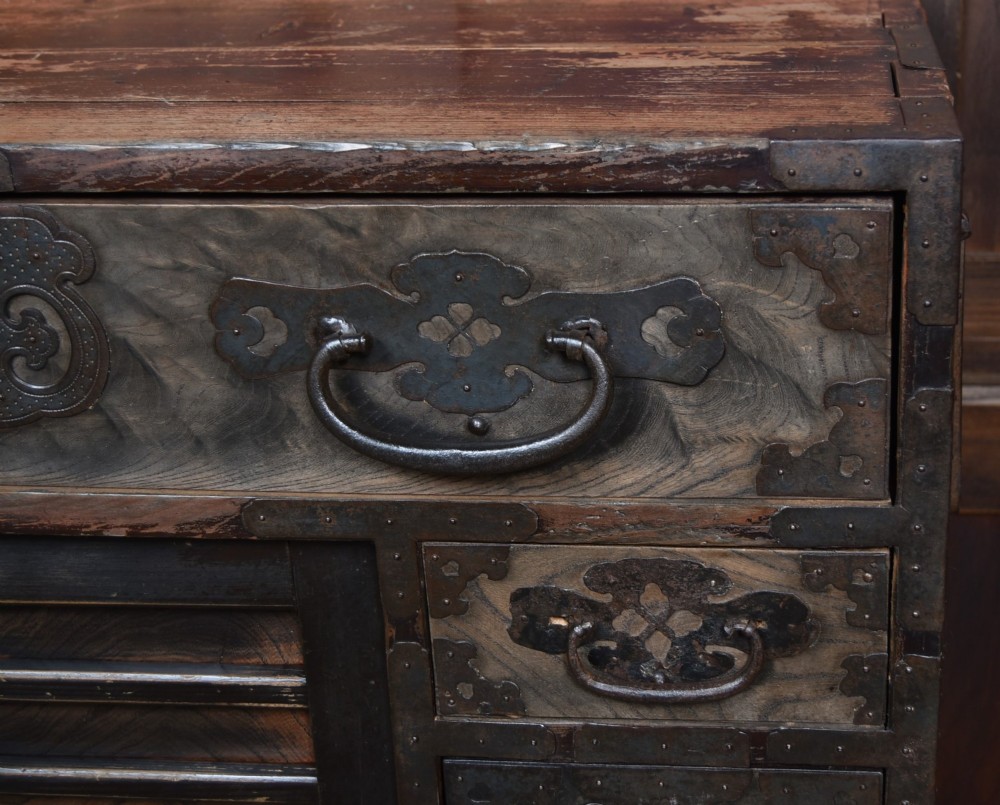 A Japanese tansu wooden chest featuring multiple drawers, sliding louvered doors, a small lockable door, and dark iron corner plates and drop handles. View III