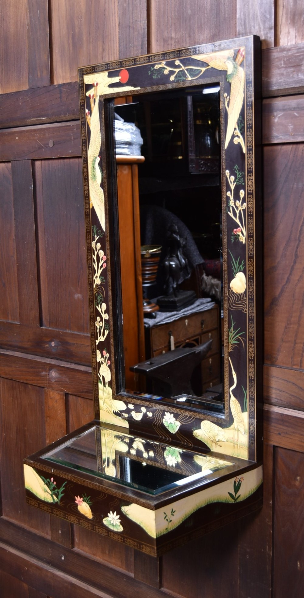 A tall black lacquered rectangular wall mirror featuring an integrated bottom shelf and painted borders with cranes, lotus blossoms, and botanical details. View X
