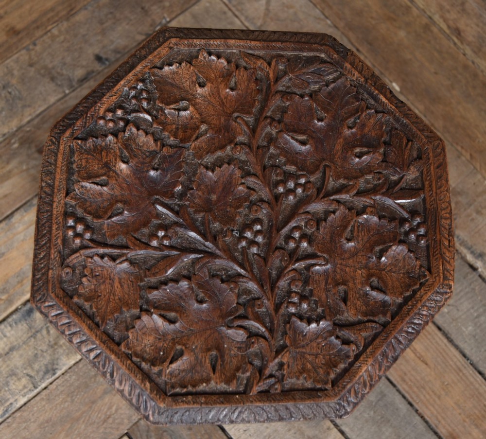 An octagonal dark hardwood side table featuring deep relief foliate carving across the top and openwork pierced panels on the folding base. View IV