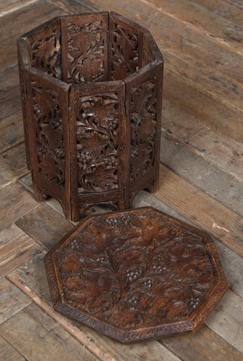 An octagonal dark hardwood side table featuring deep relief foliate carving across the top and openwork pierced panels on the folding base. View V