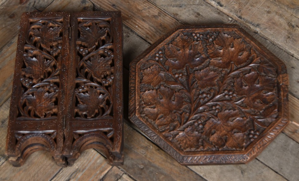An octagonal dark hardwood side table featuring deep relief foliate carving across the top and openwork pierced panels on the folding base. View VI