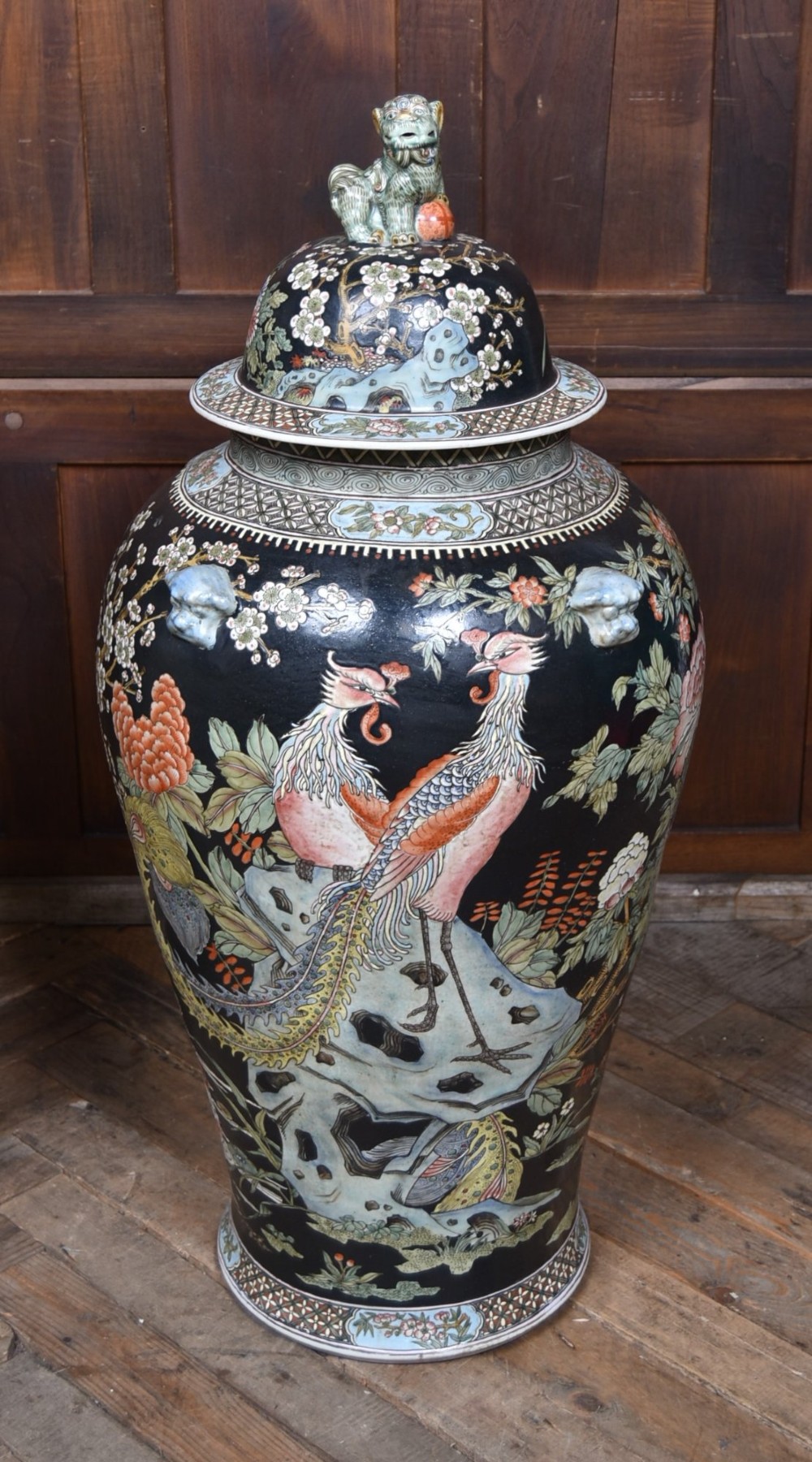 A pair of large black-ground Chinese porcelain floor jars with domed lids topped with foo dog finials and painted peacock, floral, and rockery motifs. View V