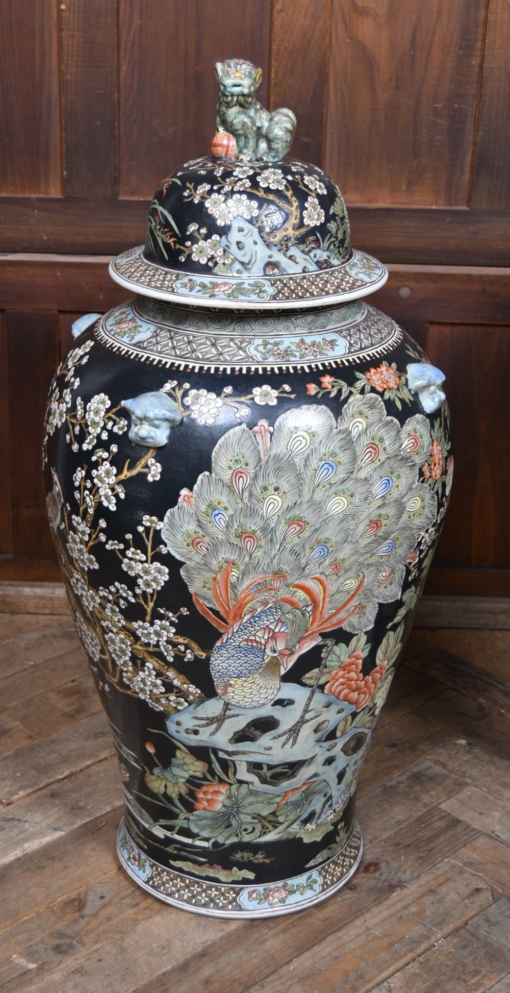 A pair of large black-ground Chinese porcelain floor jars with domed lids topped with foo dog finials and painted peacock, floral, and rockery motifs. View VI