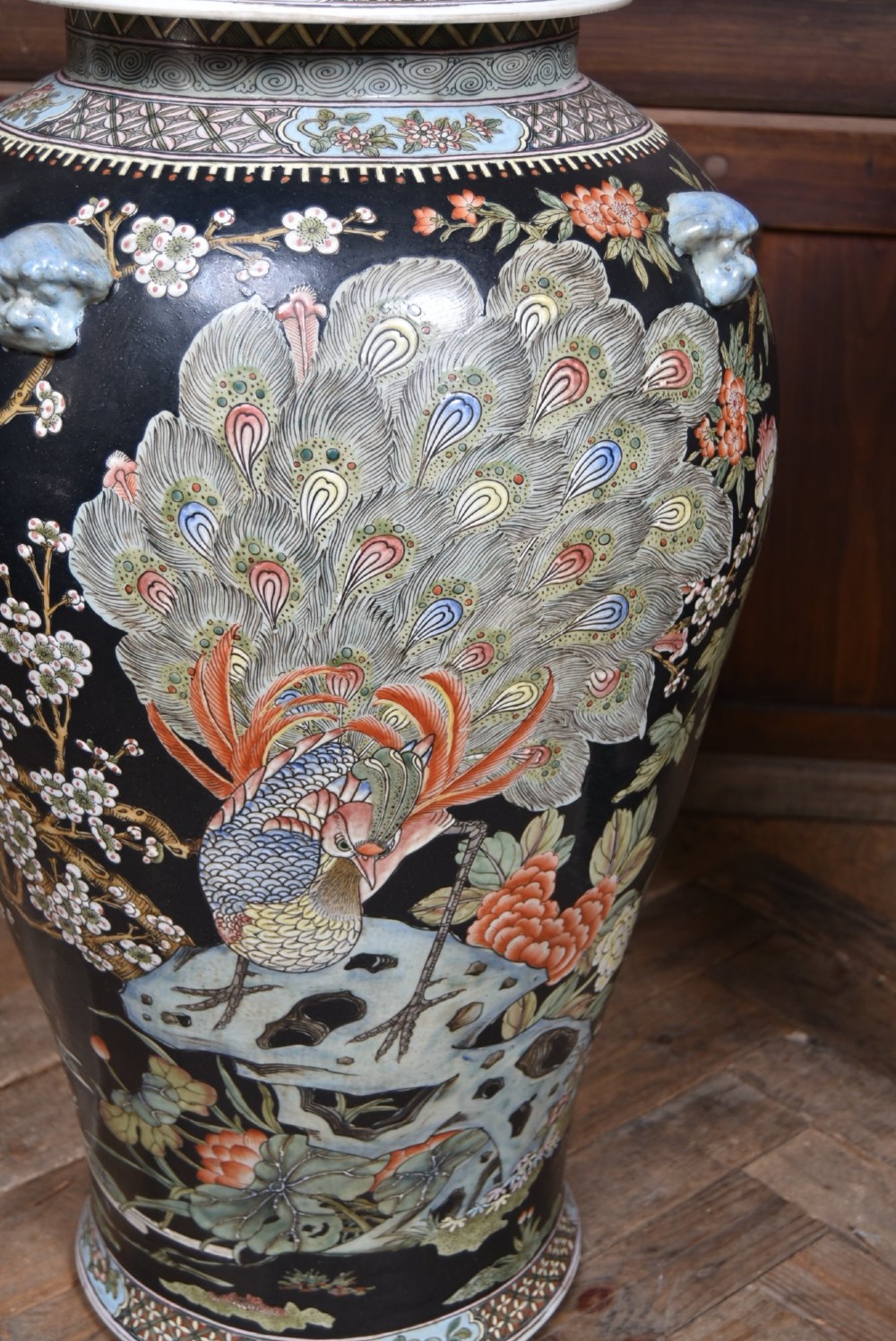 A pair of large black-ground Chinese porcelain floor jars with domed lids topped with foo dog finials and painted peacock, floral, and rockery motifs. View X