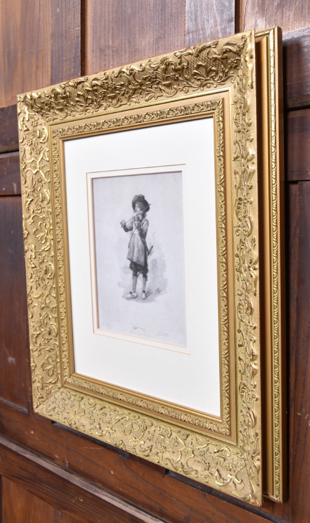 A framed monochrome print depicting a young violinist in period costume, set within a cream mount and an ornate gilded frame. View IX