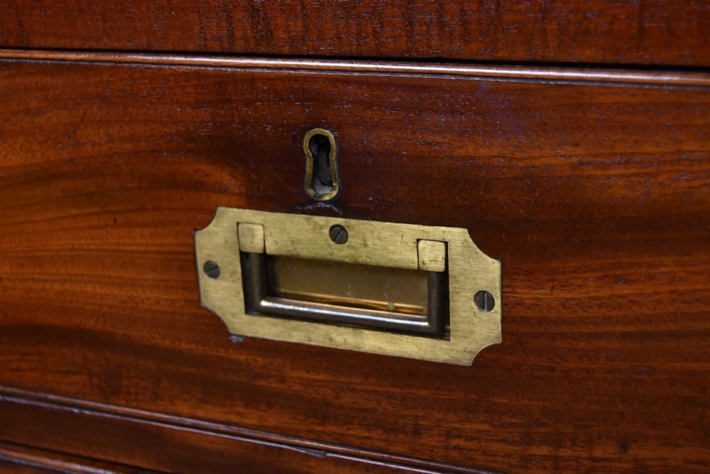 A 19th-century mahogany campaign chest of drawers featuring flush brass handles, corner brackets, and a two-section design. View IV