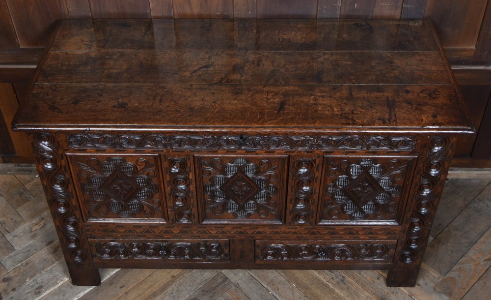 An 18th-century dark oak coffer featuring three carved panels, geometric marquetry inlay, and two lower drawers. View II