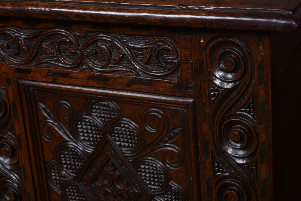 An 18th-century dark oak coffer featuring three carved panels, geometric marquetry inlay, and two lower drawers. View V