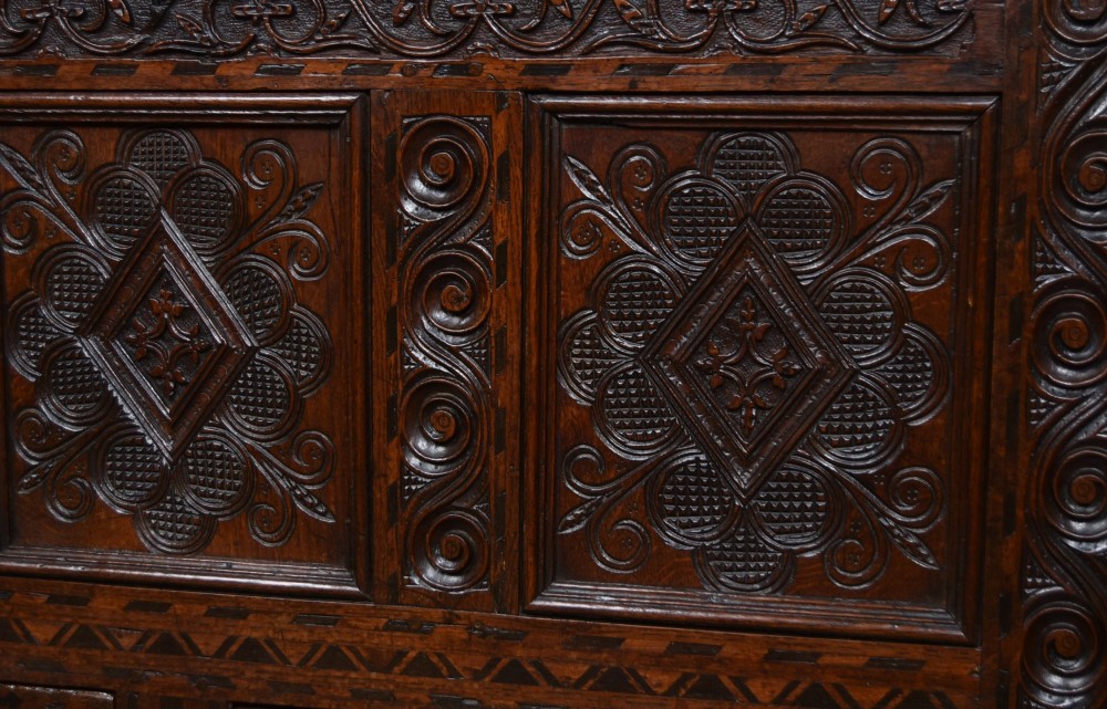 An 18th-century dark oak coffer featuring three carved panels, geometric marquetry inlay, and two lower drawers. View VI