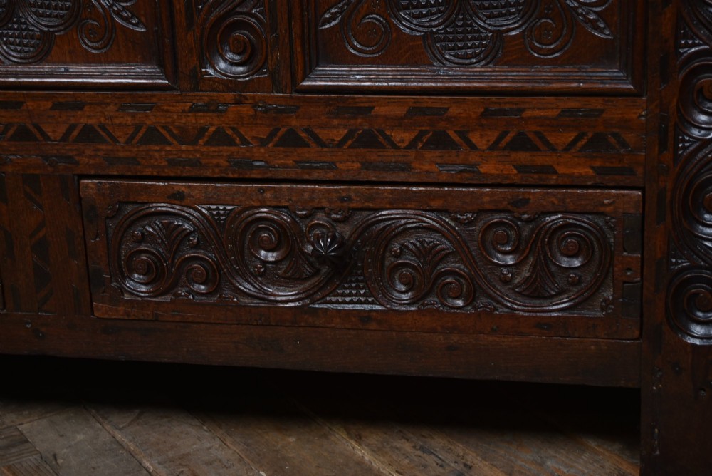 An 18th-century dark oak coffer featuring three carved panels, geometric marquetry inlay, and two lower drawers. View VII