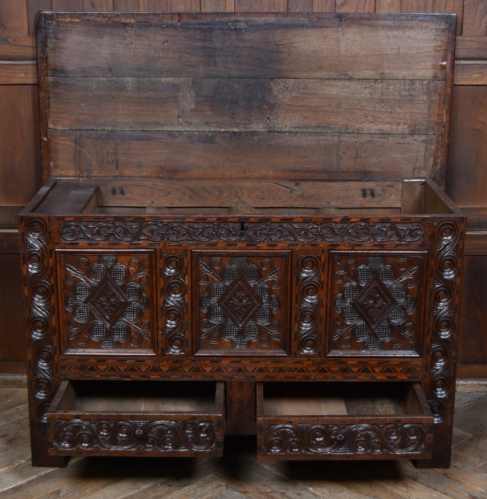 An 18th-century dark oak coffer featuring three carved panels, geometric marquetry inlay, and two lower drawers. View VIII