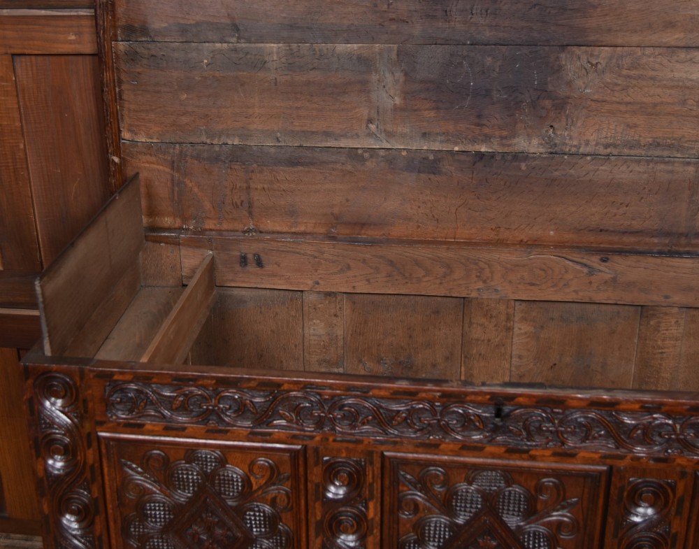 An 18th-century dark oak coffer featuring three carved panels, geometric marquetry inlay, and two lower drawers. View IX