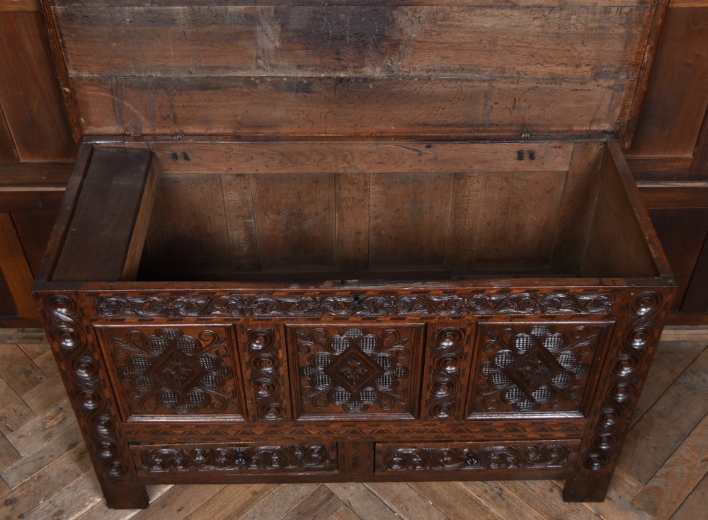 An 18th-century dark oak coffer featuring three carved panels, geometric marquetry inlay, and two lower drawers. View X