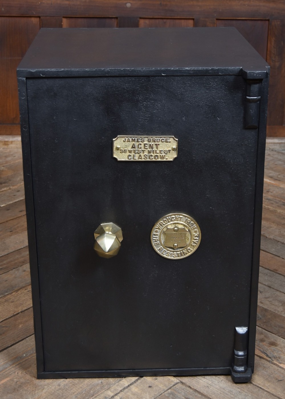 A heavy black painted iron safe featuring a rectangular body, a brass maker plaque for James Bruce of Glasgow, a faceted brass handle, and a brass fire-resisting emblem. View II