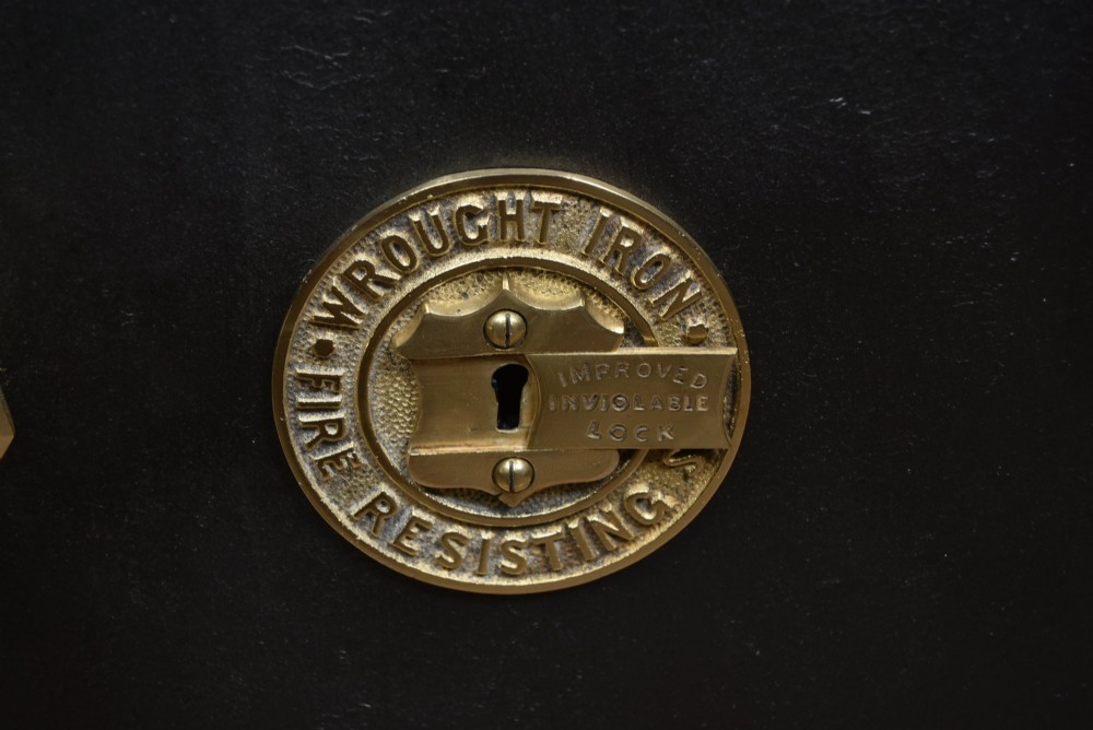 A heavy black painted iron safe featuring a rectangular body, a brass maker plaque for James Bruce of Glasgow, a faceted brass handle, and a brass fire-resisting emblem. View V