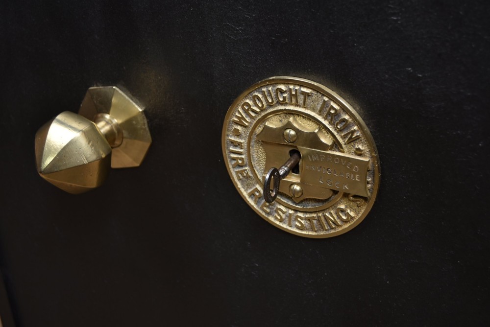 A heavy black painted iron safe featuring a rectangular body, a brass maker plaque for James Bruce of Glasgow, a faceted brass handle, and a brass fire-resisting emblem. View VI