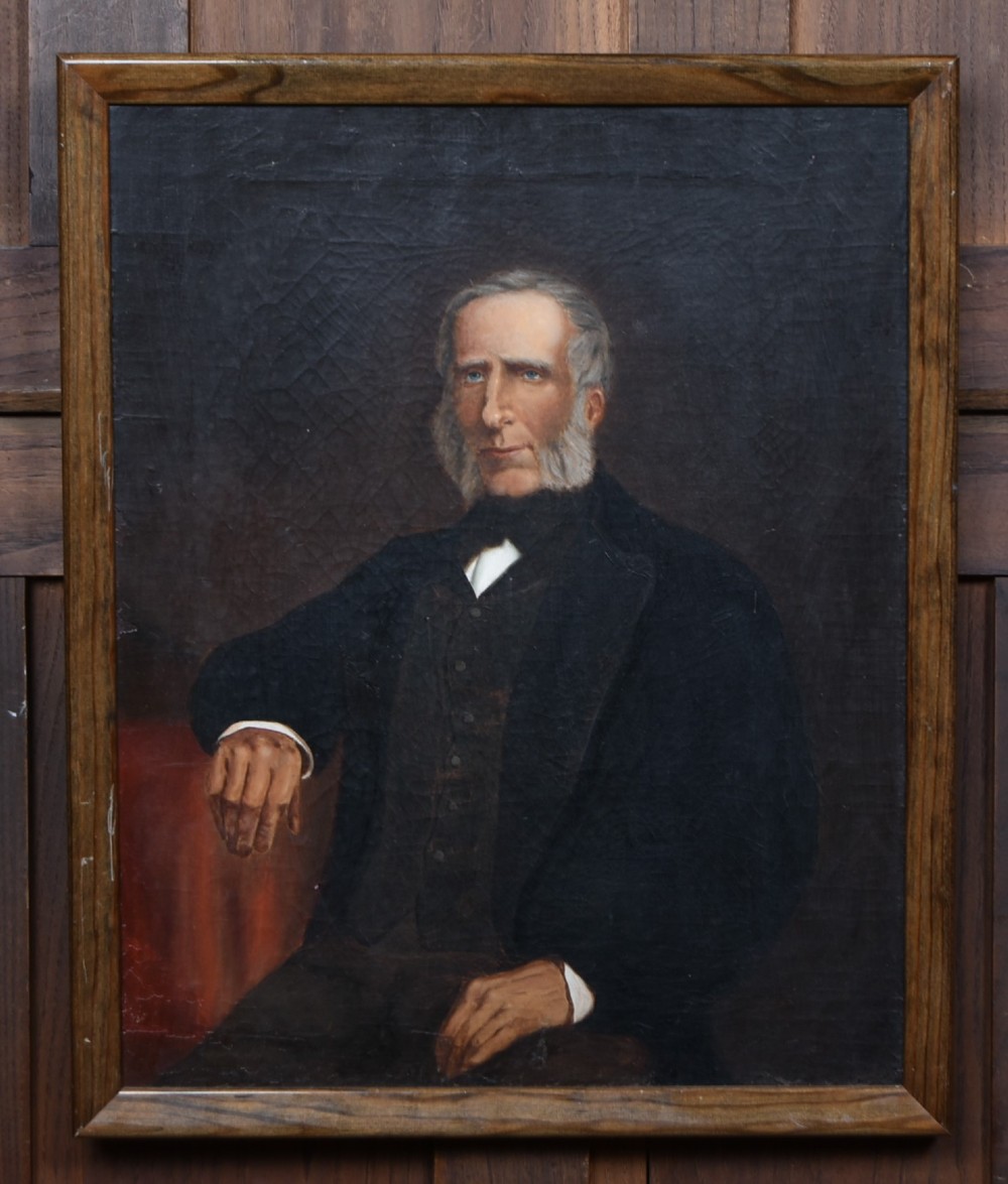A nineteenth-century oil painting depicting a seated gentleman with sideburns wearing a black coat, framed in a simple dark wooden border. View II
