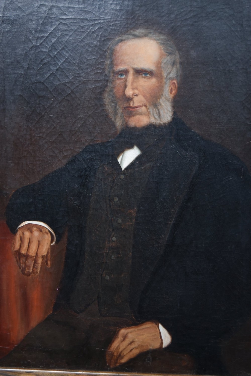 A nineteenth-century oil painting depicting a seated gentleman with sideburns wearing a black coat, framed in a simple dark wooden border. View IV