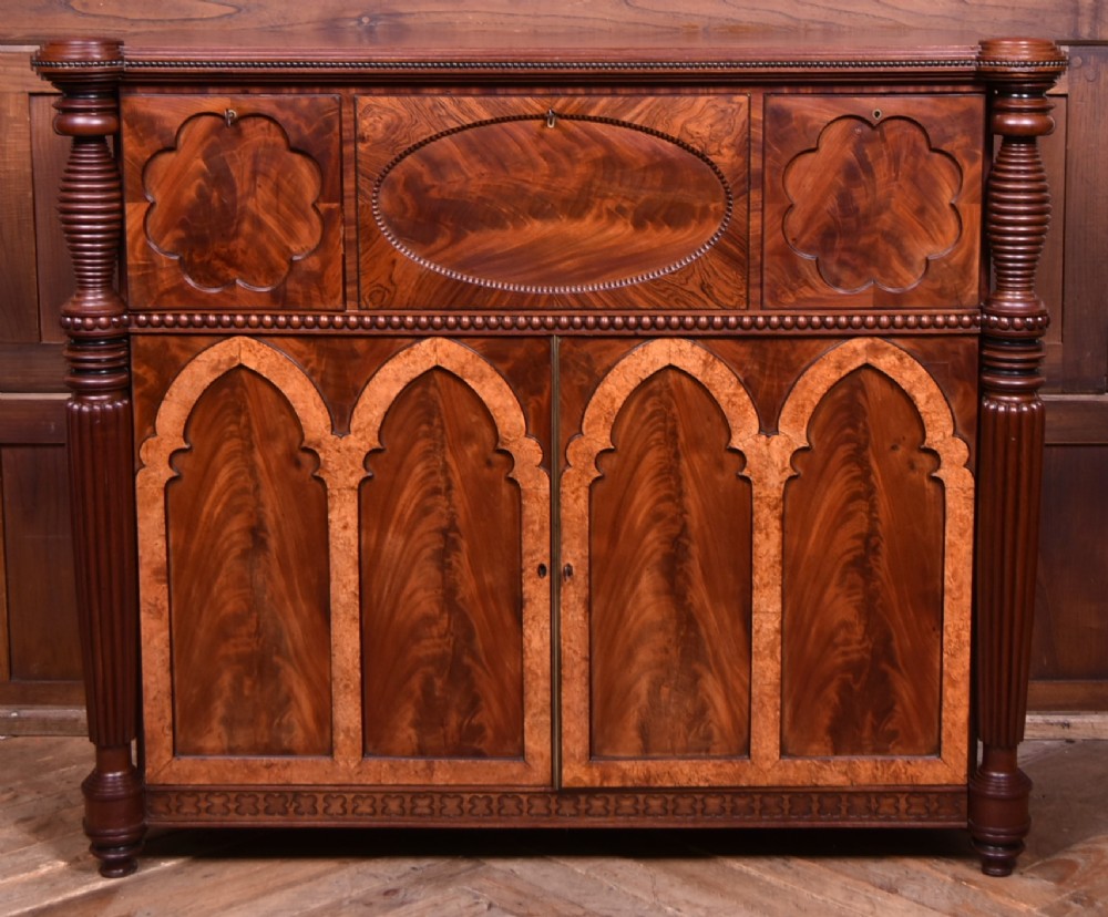 A Victorian mahogany secretaire cabinet featuring Gothic arch decorative panels, turned columns on either side, and flame mahogany veneers.