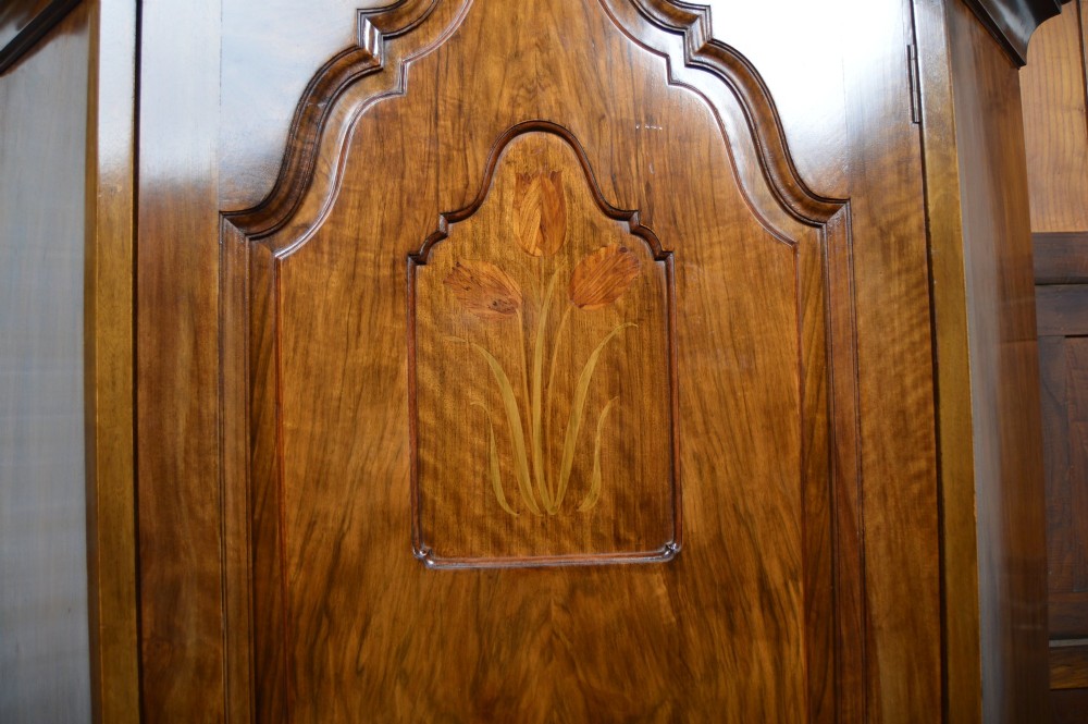 An antique Art Nouveau corner wardrobe crafted from warm walnut wood with an arched pediment, a single panel door featuring floral marquetry, and a shaped plinth base. View V
