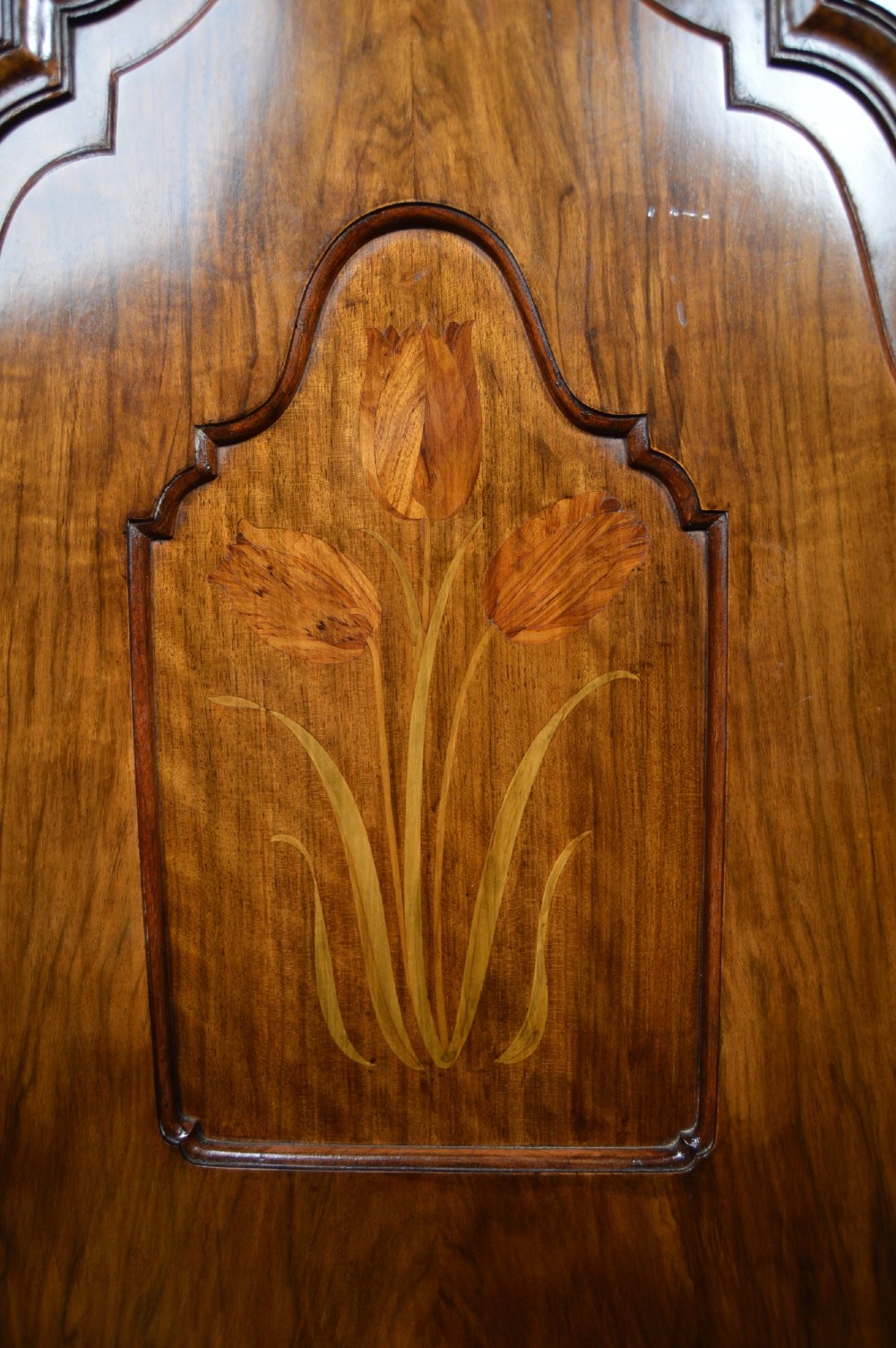 An antique Art Nouveau corner wardrobe crafted from warm walnut wood with an arched pediment, a single panel door featuring floral marquetry, and a shaped plinth base. View VI