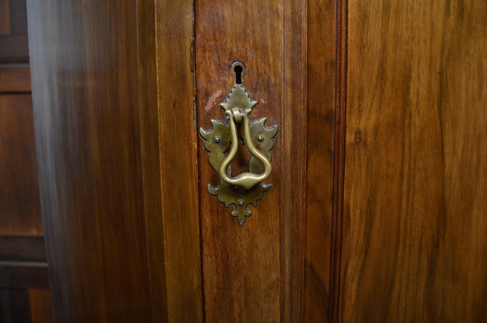 An antique Art Nouveau corner wardrobe crafted from warm walnut wood with an arched pediment, a single panel door featuring floral marquetry, and a shaped plinth base. View VII