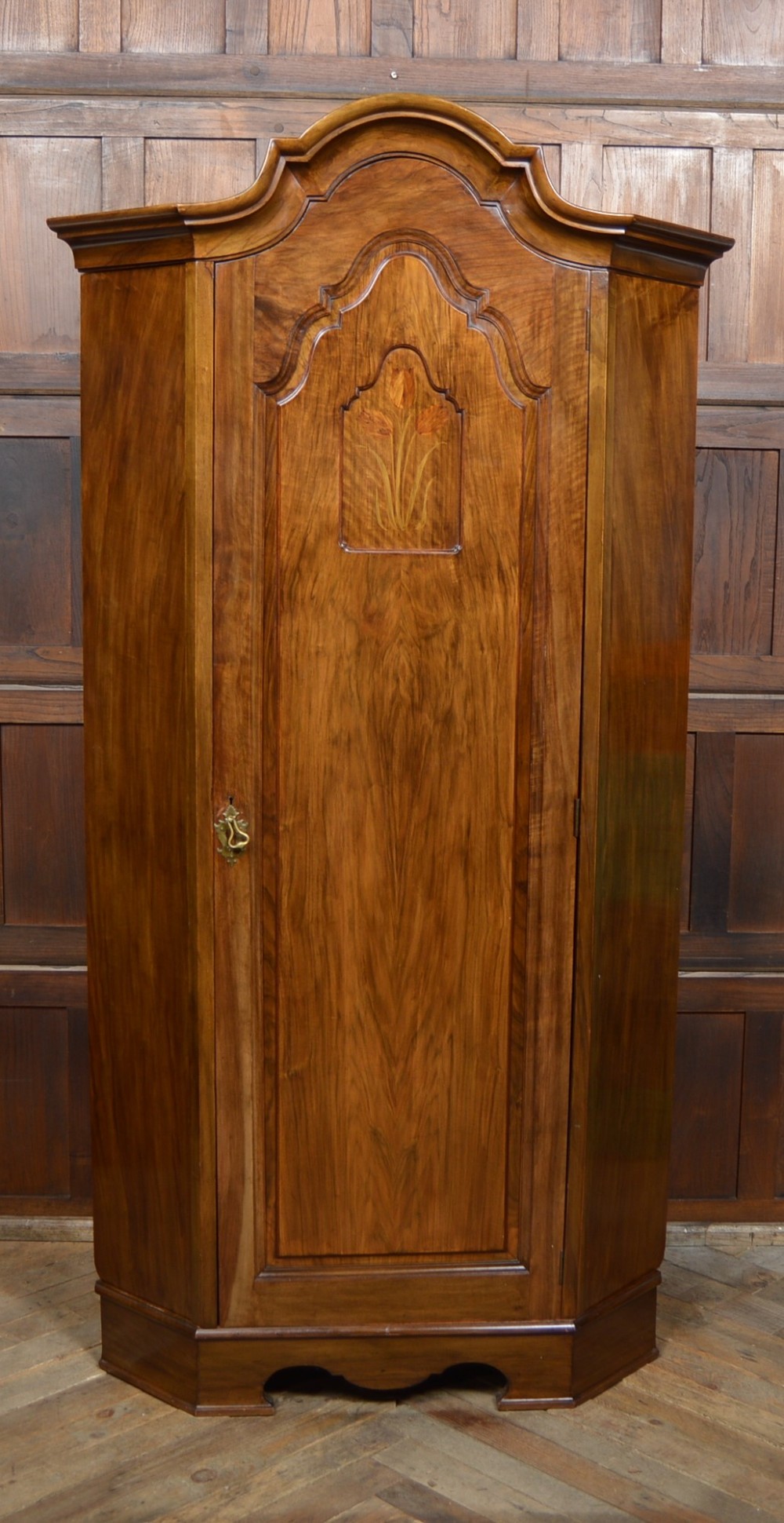 An antique Art Nouveau corner wardrobe crafted from warm walnut wood with an arched pediment, a single panel door featuring floral marquetry, and a shaped plinth base. View IX