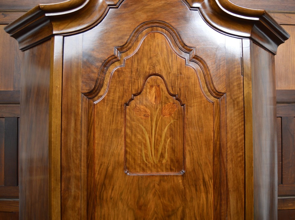 An antique Art Nouveau corner wardrobe crafted from warm walnut wood with an arched pediment, a single panel door featuring floral marquetry, and a shaped plinth base. View X
