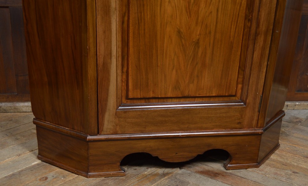 An antique Art Nouveau corner wardrobe crafted from warm walnut wood with an arched pediment, a single panel door featuring floral marquetry, and a shaped plinth base. View XI