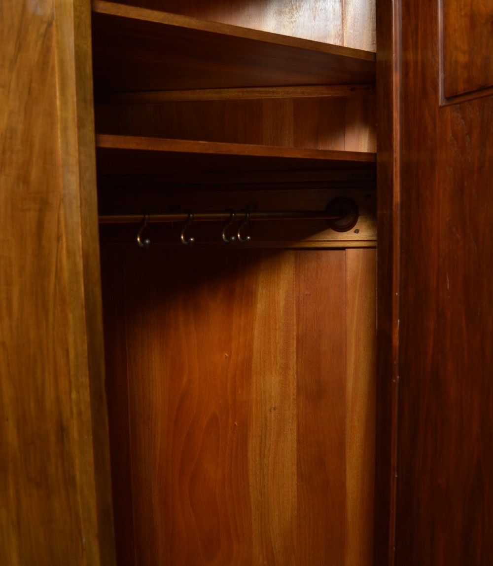 An antique Art Nouveau corner wardrobe crafted from warm walnut wood with an arched pediment, a single panel door featuring floral marquetry, and a shaped plinth base. View XV